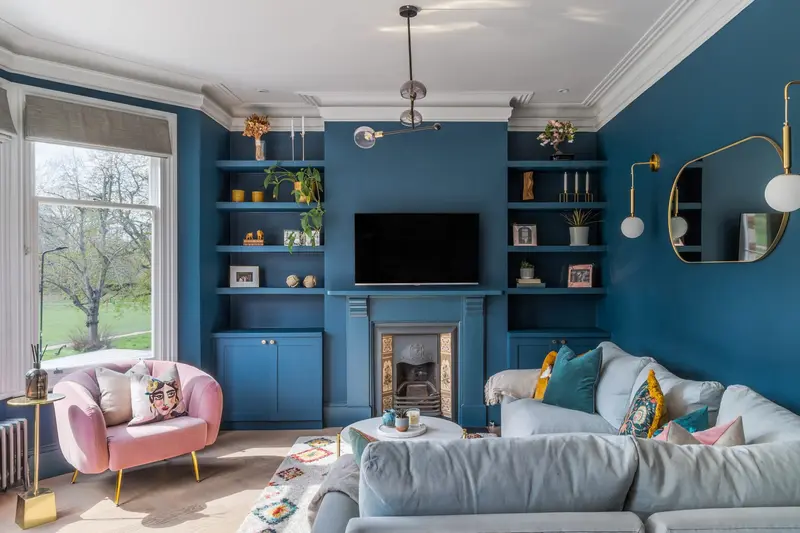 Teal living room with built-in shelves, pink armchair and grey sofa