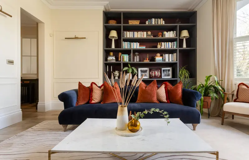 Balham living room with a navy velvet sofa, burnt orange cushions and built-in bookcase