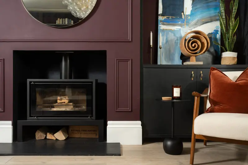 Aubergine fireplace wall with a wood-burning stove and rust armchair