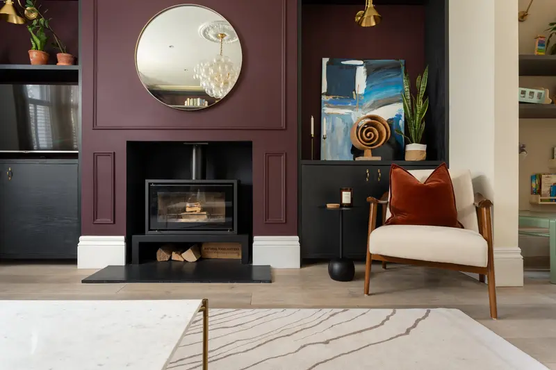 Aubergine fireplace wall with a round mirror and boucle armchair
