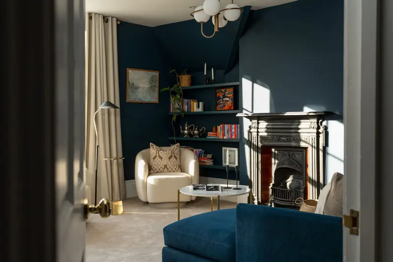 Navy sitting room with boucle chair and built-in shelving, seen through the doorway