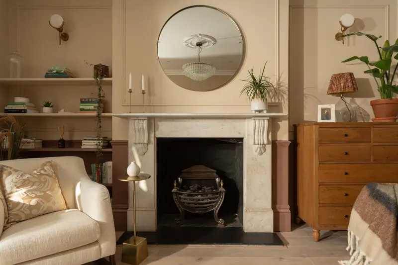 Bedroom fireplace with a cream armchair and round mirror