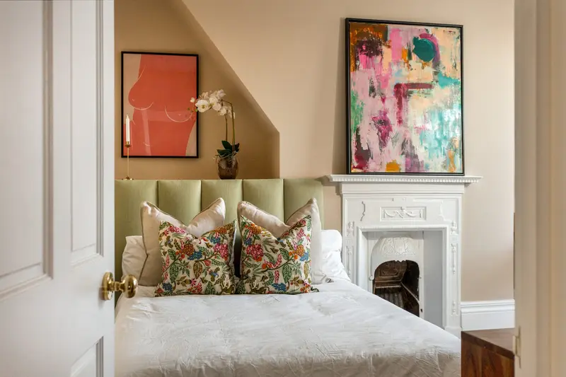 Guest bedroom with green headboard, patterned cushions and abstract art