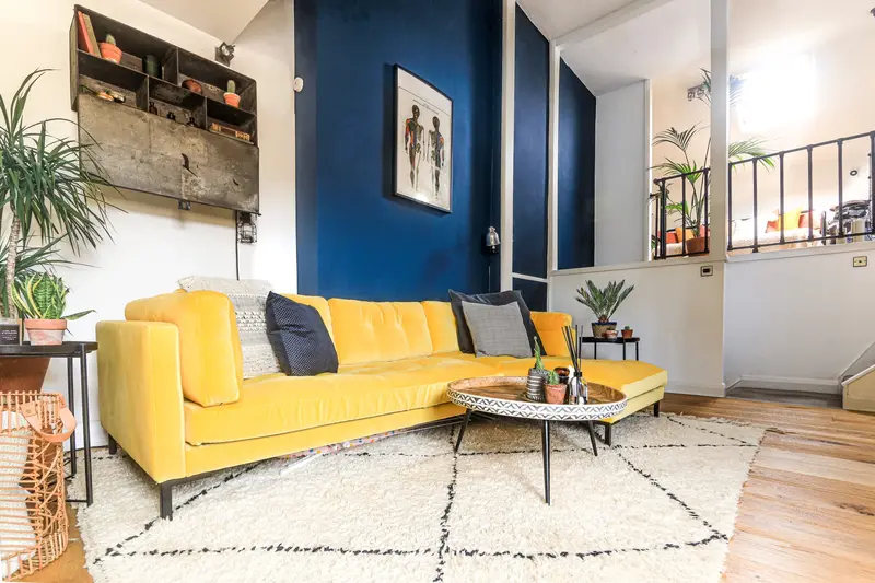 Living room with a mustard sofa, navy wall and Berber rug