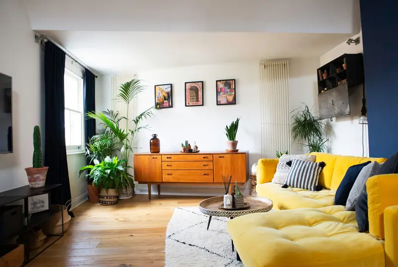 Living room with a mid-century sideboard, yellow sofa and palms