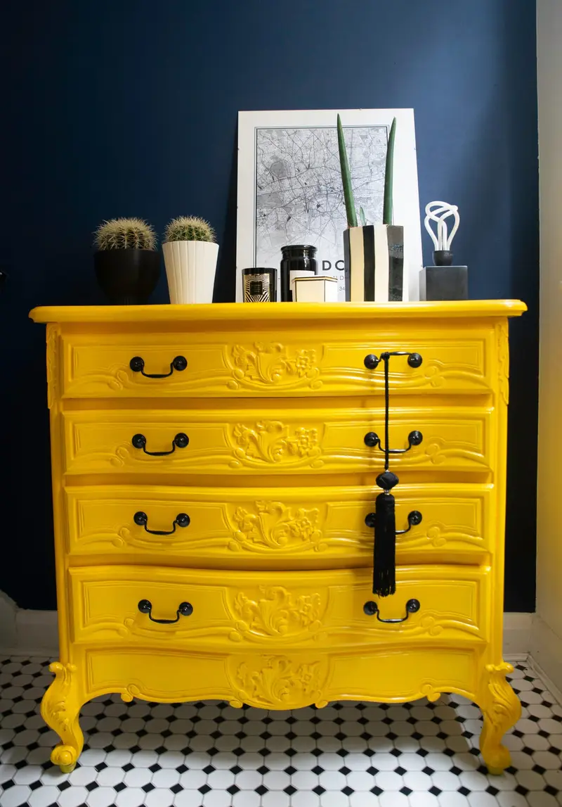 French chest of drawers painted yellow against a navy wall