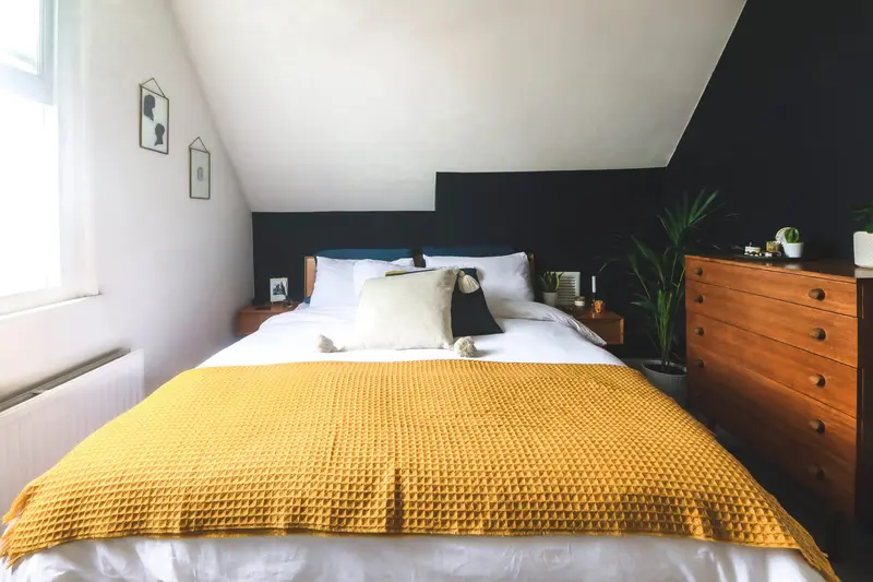 Loft bedroom with mustard throw and teak chest of drawers