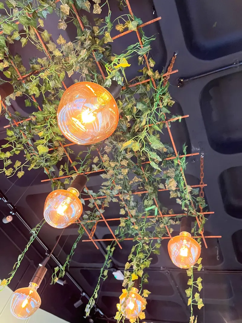 Ceiling crown of rebar and chains draped with greenery and warm bulbs