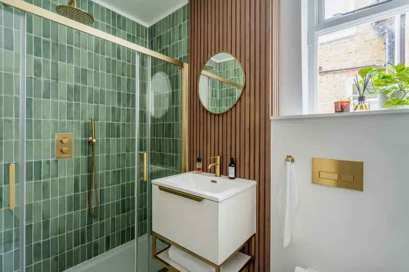 Green-tiled bathroom with fluted wood panelling and brass fittings