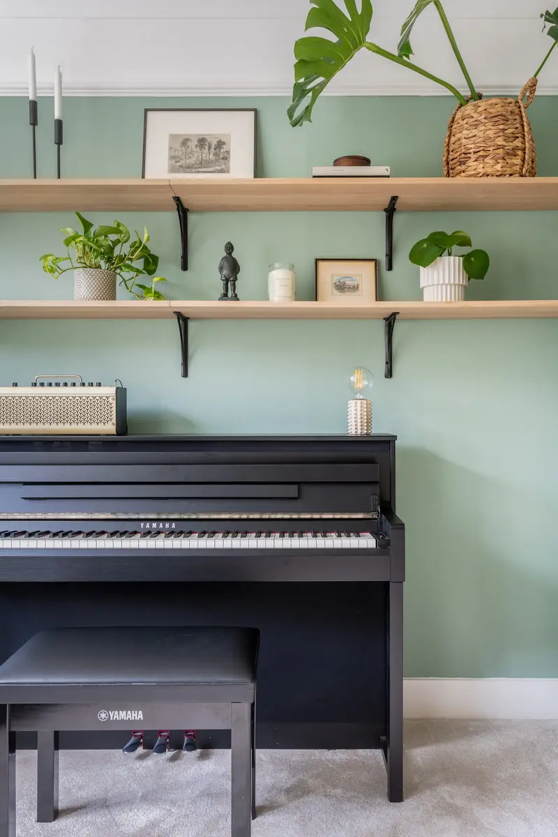 Sage-green music corner with a piano and floating shelves