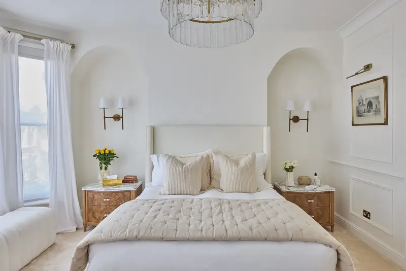 Upholstered bed flanked by burr-wood bedside tables and brass wall lights
