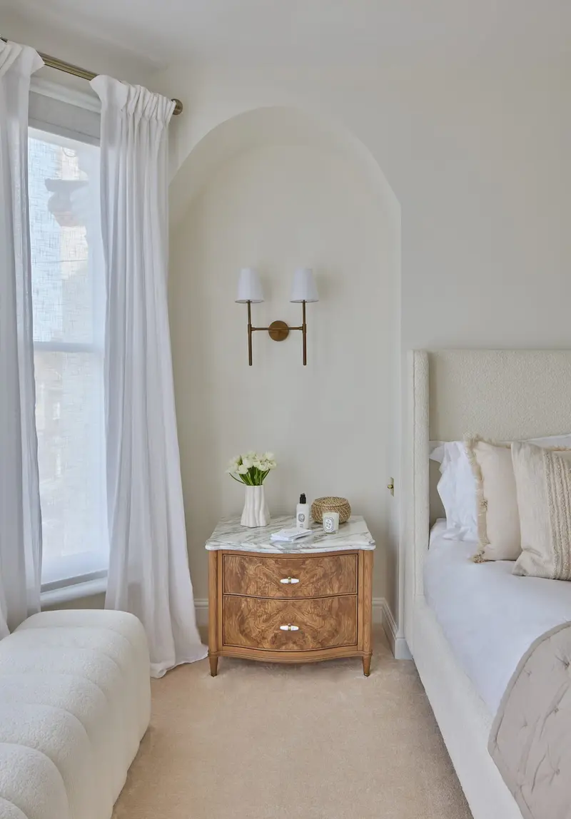 Bedroom corner with sheer curtains, brass wall lights and a bedside chest