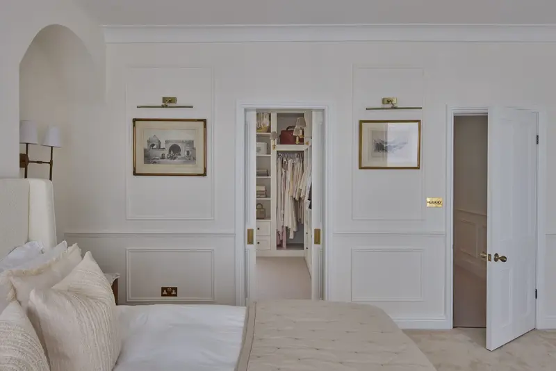 Panelled bedroom wall with picture lights leading through to a dressing room