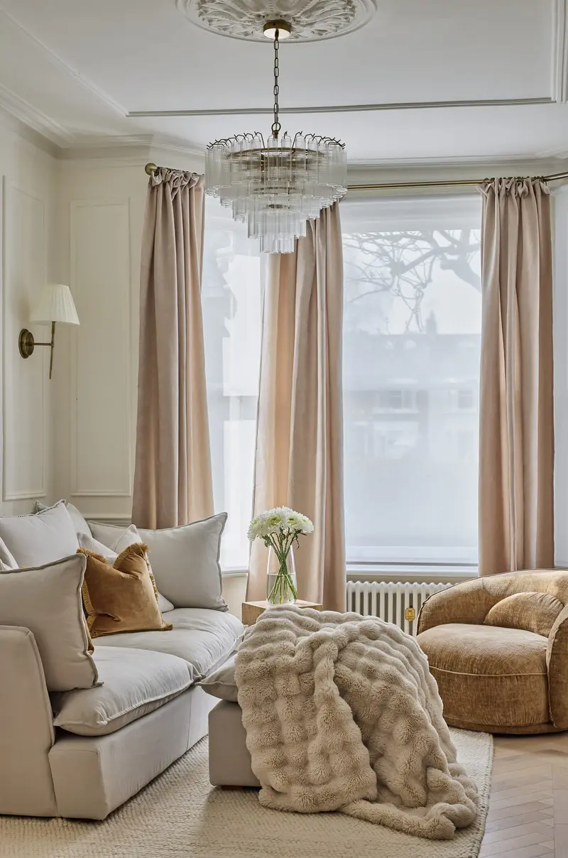 Cream sofa with a faux-fur throw beneath tall windows and a chandelier