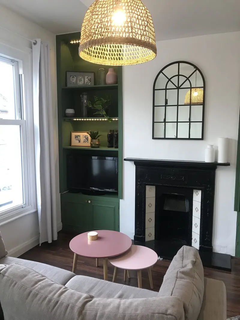 Living room with a sage alcove unit, black fireplace and arched mirror